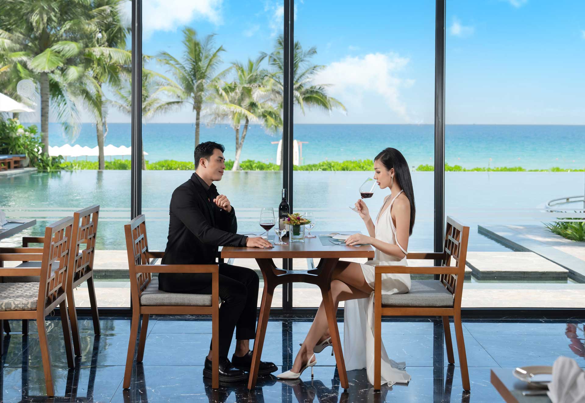 1 đôi nam nữ đang ngồi ăn uống tại nhà hàng cạnh hồ bơi
